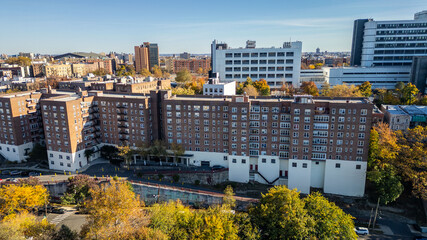 Fototapeta premium This location in the Bronx offers stunning views of lush greenery, a picturesque lake, and urban structures. Framed by the river, it showcases iconic bridges and the New York City skyline in the dista