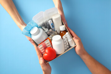 Hands holding a healthcare kit with medication, pills, thermometer, and bandages on a blue...