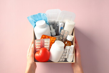 Box with essential healthcare kit with medication, pills, bandages, and face mask in female hands....