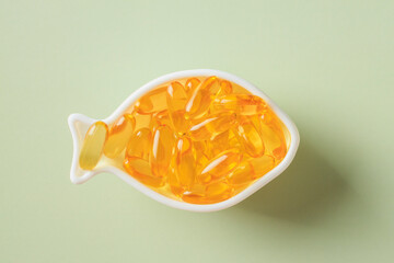 Fish-shaped dish filled with translucent orange omega-3 capsules on a light green background