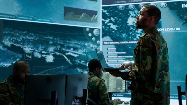 Military officers work in a high tech army control tower base, managing surveillance imagery from cctv satellite. Soldiers handle data protection to ensure national security. Camera A.