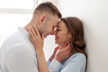 young couple in love stands close, holds the neck and looks into the eyes before kissing, the man passionately kisses the woman at home and smiles, close-up