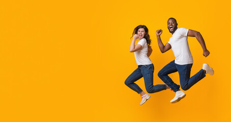 Funny interracial couple jumping in the air, running fast to big sales, hurry to come in time,...