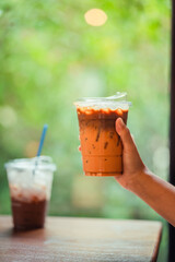 hand of woman holding a take-out iced thai tea with espresso on wooden table