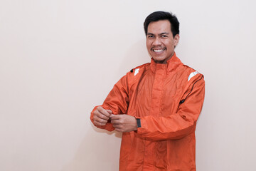 Smiling Southeast Asian man wearing orange raincoat with hand for button up the sleeves looking at...