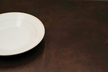 Empty white ceramic plate with orange circle isolated on brown background, eating place setting.