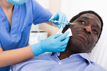 Adult african man patient of cosmetologist receiving hyaluronic acid injections in cosmetology clinic