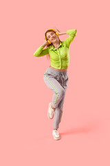 Beautiful young happy woman in headphones dancing on pink background