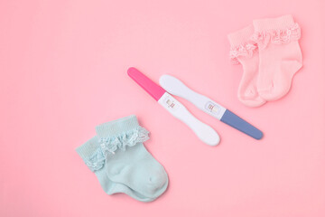 Pregnancy tests and socks on pink background, top view