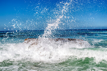 wave splashing on a giant stone in the ocean, spray bubbles in the blue sky