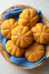 Wicker basket with tasty pumpkin shaped buns on light table, top view