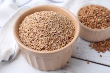 Buckwheat bran in bowl on white wooden table, closeup