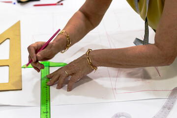A close-up of a tailor marking fabric with a pink pencil and green ruler, surrounded by tools...