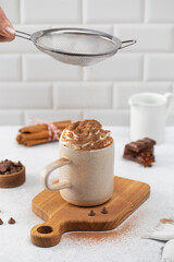 Pouring cocoa powder onto whipped cream in cup on cutting board