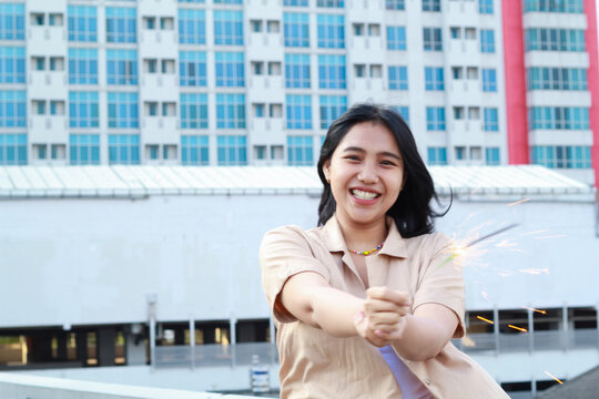 beautiful asian young woman holding sparklers firework and laughing in new year eve celebration standing in roof top outdoor with urban building background
