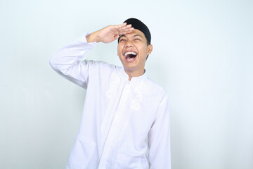 laughing asian muslim man pose look far away with hand over head isolated on white background