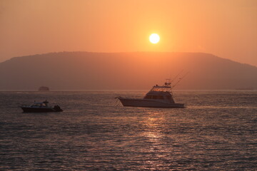Beach sunrise: orange sky, calm sea, boat, captivating beauty in nature.
