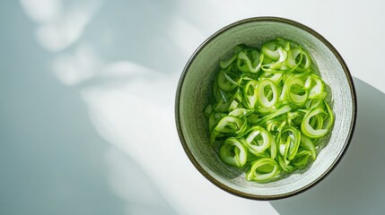 Obraz premium Top view of sliced green onions in a bowl, vivid color contrast on white