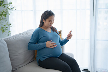Pregnant asian woman holding smartphone at home using mobile app for pregnant women Positive life moment in pregnancy time