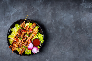 Grilled chicken teriyaki on wooden skewer with hot sauce.