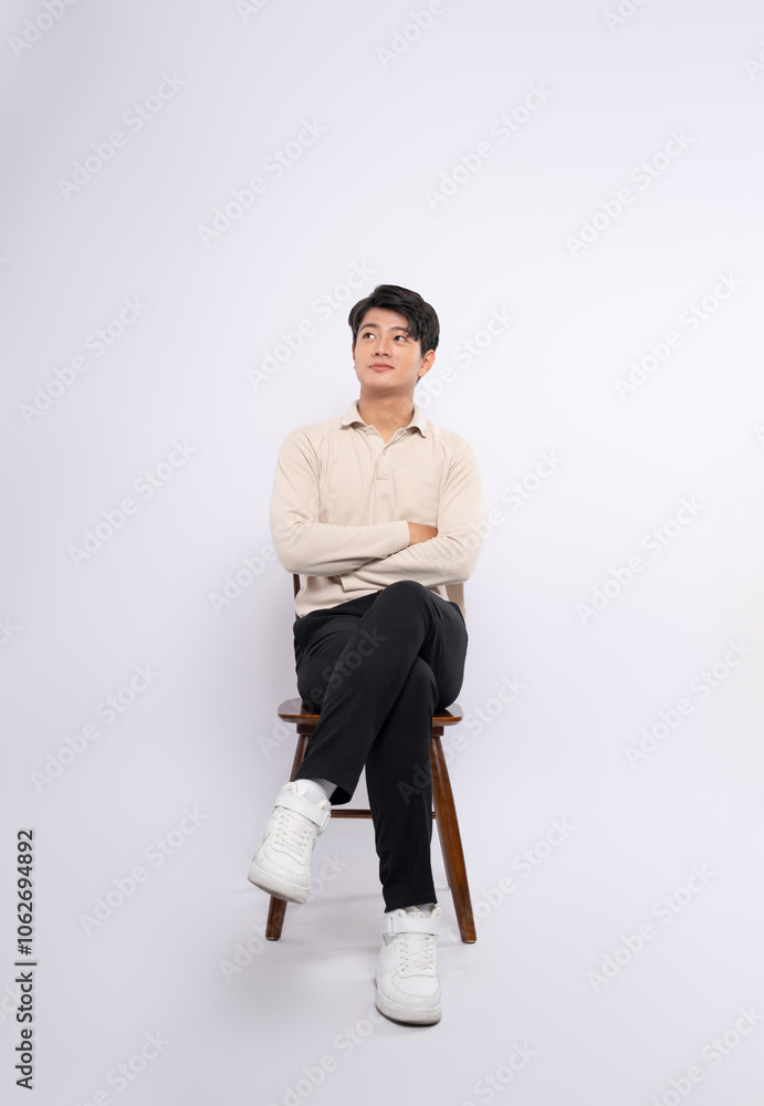 Wall mural Full body image of a young businessman sitting in a chair and posing on a white background