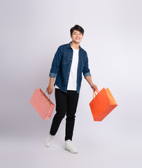 Full body image of young Asian man holding shopping bag and posing on white background
