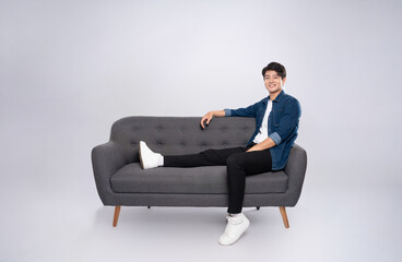 Full body image of young Asian man posing on sofa on white background