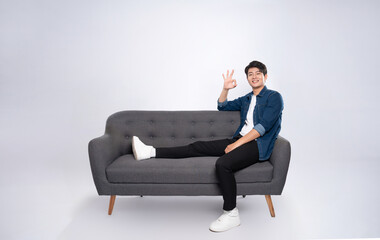 Full body image of young Asian man posing on sofa on white background