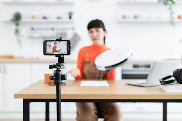 Caucasian female blogger demonstrates and reviews new robot vacuum cleaner online. Young adult content creator showcases features and usability of latest technology.
