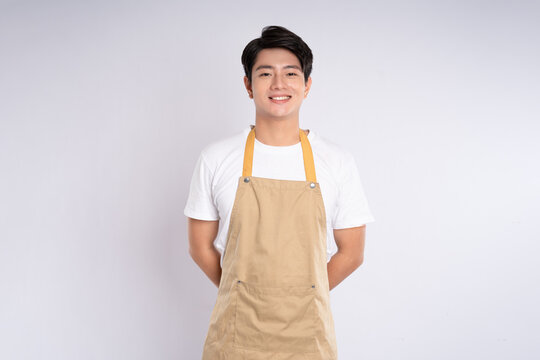 Portrait of young asian man wearing apron and posing on white background