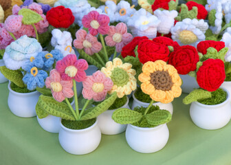 Close up on many beautiful crochet flowers in small white plastic pots on a green table. Hand crafted.
