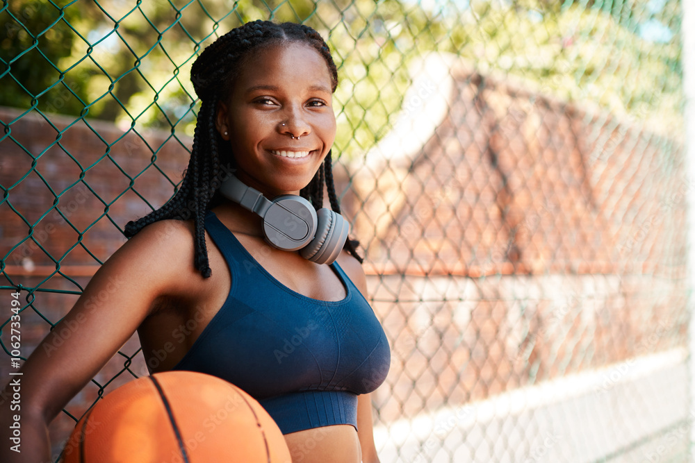 Wall mural Black woman, basketball court and smile in portrait with ball as athlete for challenge or exercise. Female person, headphones and fence for competition, match or game for sports or training as player