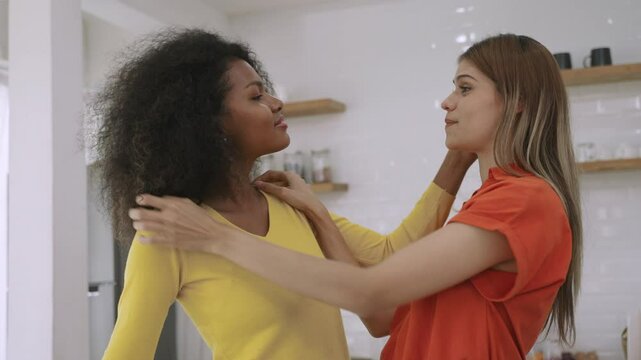 Happy interracial lesbian couple standing smiling and hugging while showing their love and sincerity to each other in the kitchen room at home. Romantic of black female and girlfriend LGBTQ pride. 