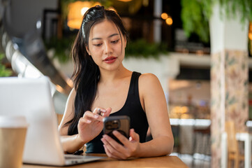 A woman is working remotely from a coffee shop, sending messages or reading chat on her smartphone.