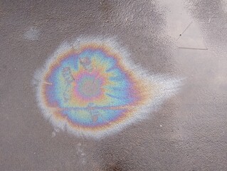 A wet road with spilled gasoline creates an abstract display, as iridescent colors of blue, purple,...