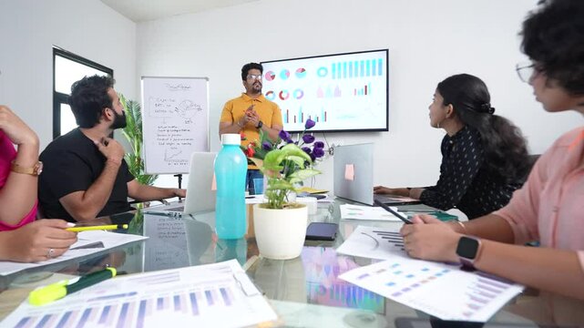 young indian man entrepreneur present business financial data on TV display screen at workplace to colleagues for a start-up project. sales, analysis and strategy, Growth of company.