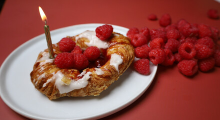 Delicious sweet dessert with raspberry and fire candle on the white plate and red background 
