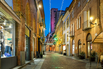 Obraz premium Cobblestone street and old buildings illuminated with Christmas lights in the evening in Alba, Italy.