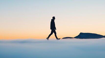 Silhouette of a man walking above the clouds at sunrise.