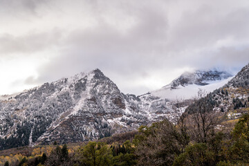Fototapeta premium Snow-covered mountain peaks with forested slopes under cloudy sky