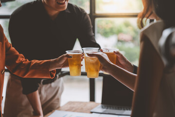 Team of business men and women sitting at desks with documents, graphs, charts, holding glasses of champagne, clinking beers, celebrating a party in business success together in the office.