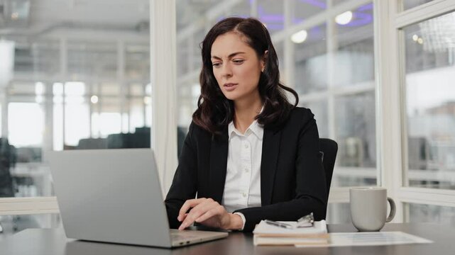 Sick businesswoman in a suit sits at her desk and works on her laptop. Lawyer has a headache and rubs her forehead. Woman is tired and overworked.