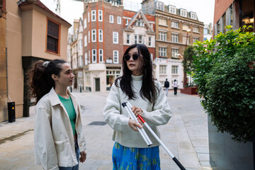 Blind woman holding white cane talking with friend in city center