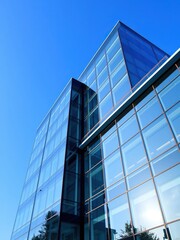 Obraz premium Modern office building with sleek glass exterior, set against a vibrant blue sky, business, reflection, modern
