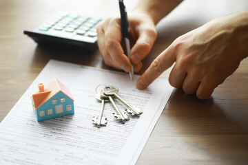 Person Signing Real Estate Contract with Keys and Calculator on the Table