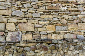 Wall of stones of different sizes, gray and light brown color. Dry masonry without cement of different styles and layers