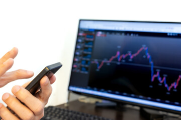 モニターで投資情報をチェックしながらスマホで取引