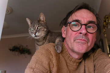 A mature man wearing glasses with cat on his shoulder