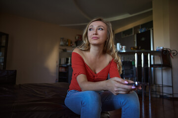 Obraz premium Serene blond woman at home relaxing on a sofa and holding smartphone