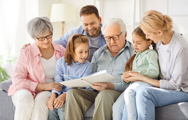 Three generations family portrait enjoying watching childhood picture album hugging beloved senior...